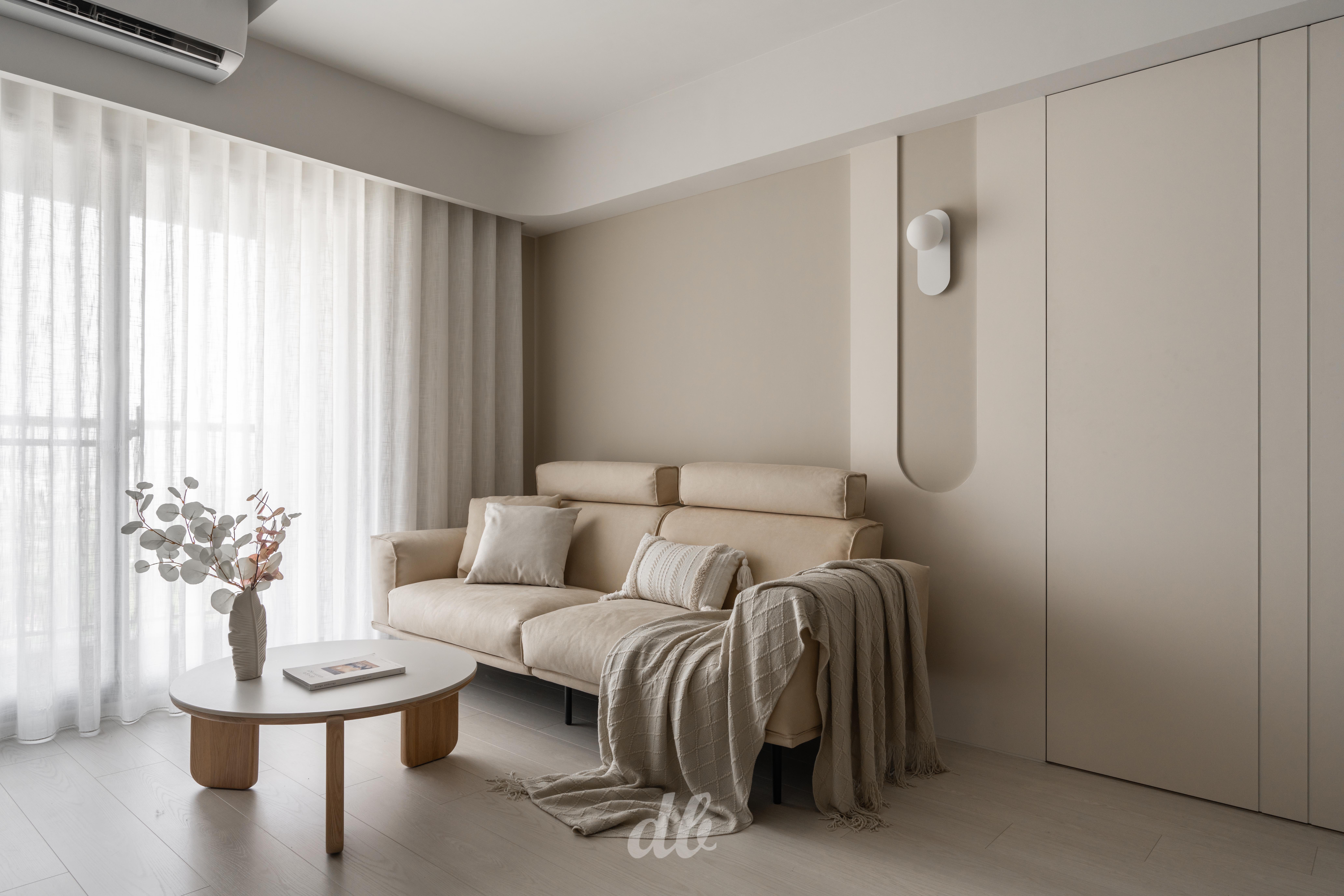 韓式奶油風客廳日造設計案例：暖米色調牆面嵌入圓弧造型壁燈，搭配柔軟布藝沙發與異材質針織毯，在紗簾柔光與低飽和色彩的映襯下，營造出具備豐富層次感且溫潤的日常居家氛圍。