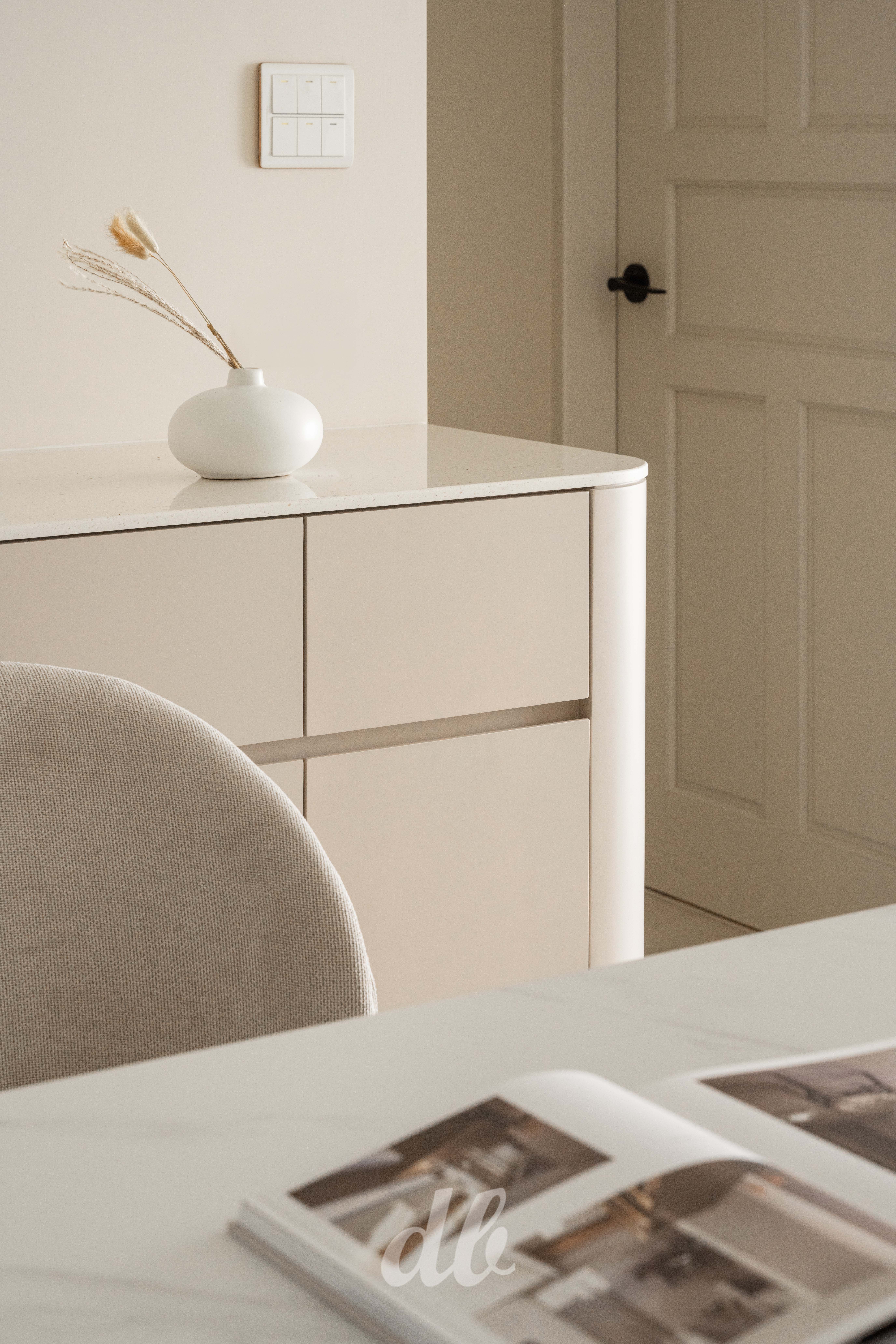 韓式奶油風餐櫃設計（日造設計案例）：溫潤米色調的圓弧收邊餐櫃，搭配白色花瓶與低飽和色彩家具，透過圓潤線條與純淨留白，具體展現韓系美學中簡約且富有生活溫度的細節質感。
