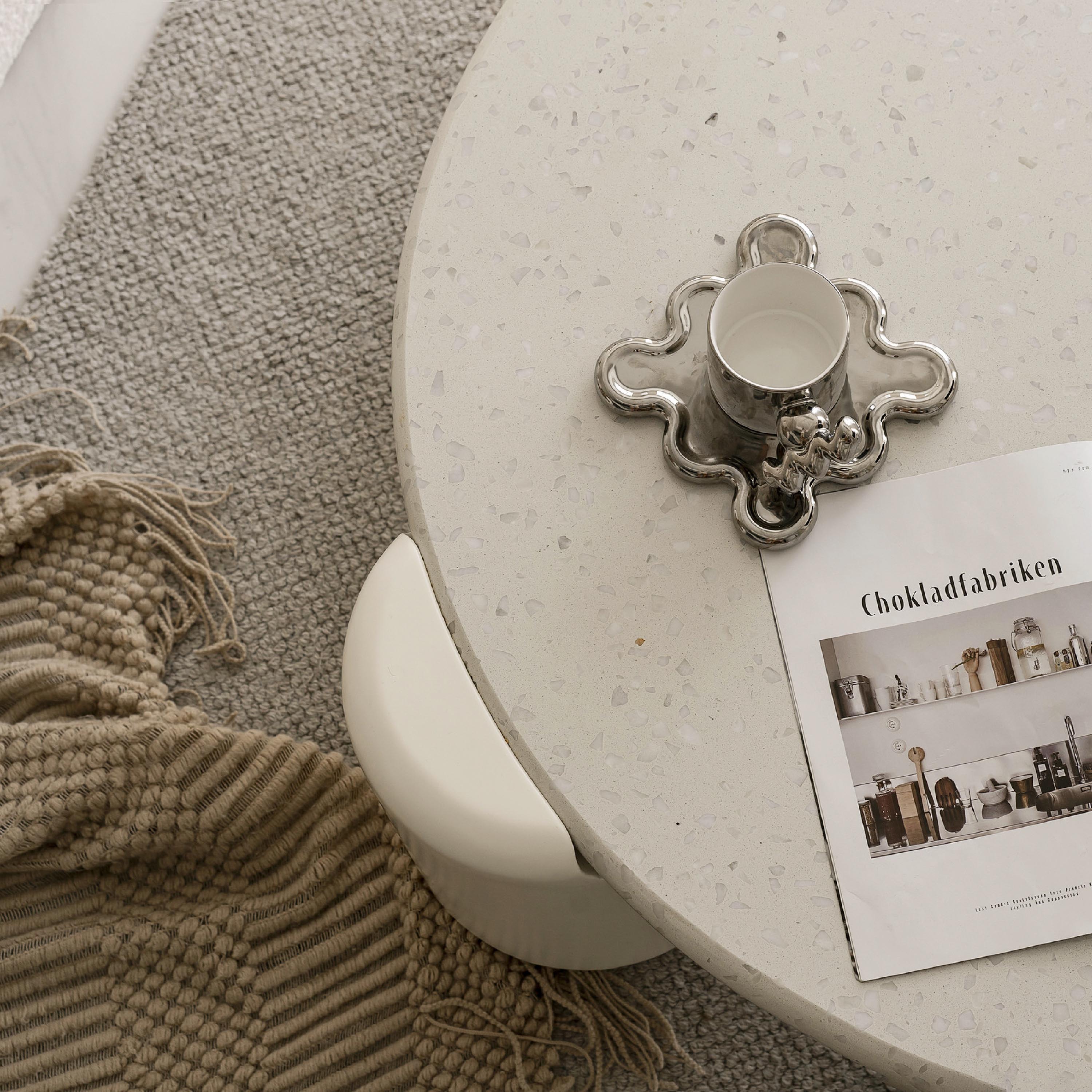 韓式奶油風軟裝材質細節：白色水磨石紋理圓桌，搭配金屬光澤的造型咖啡杯組與溫潤的針織地毯，透過異材質的疊加與低飽和配色，展現出精緻且具備生活溫度的韓系軟裝美學。