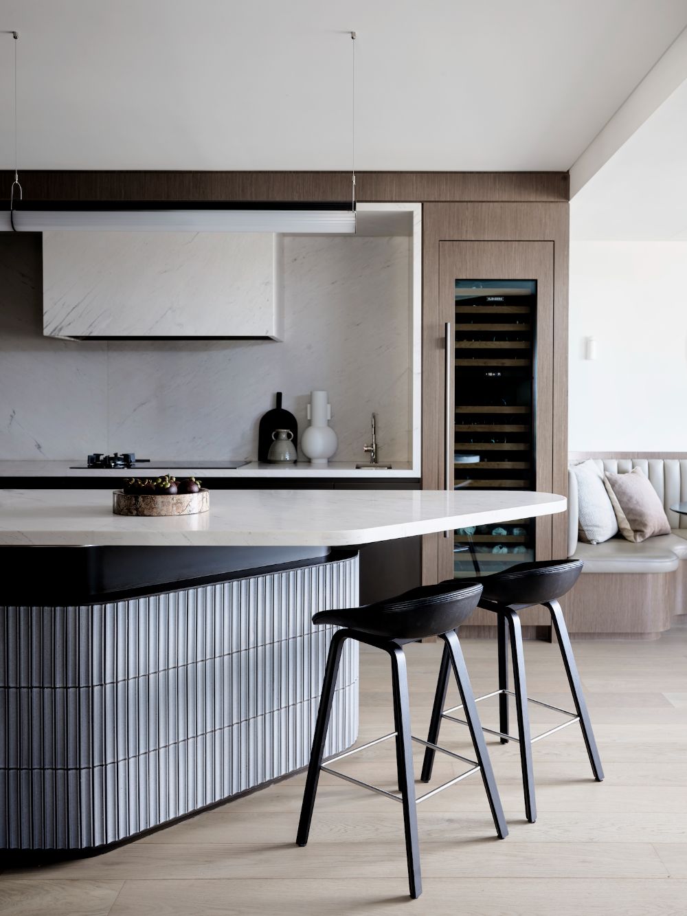 石英石中島設計案例：弧形石英石中島搭配精緻的灰色磁磚底座設計，結合嵌入式酒櫃，在黑色高腳吧台椅的襯托下，完美詮釋現代輕奢與功能主義並行的餐廚美學。